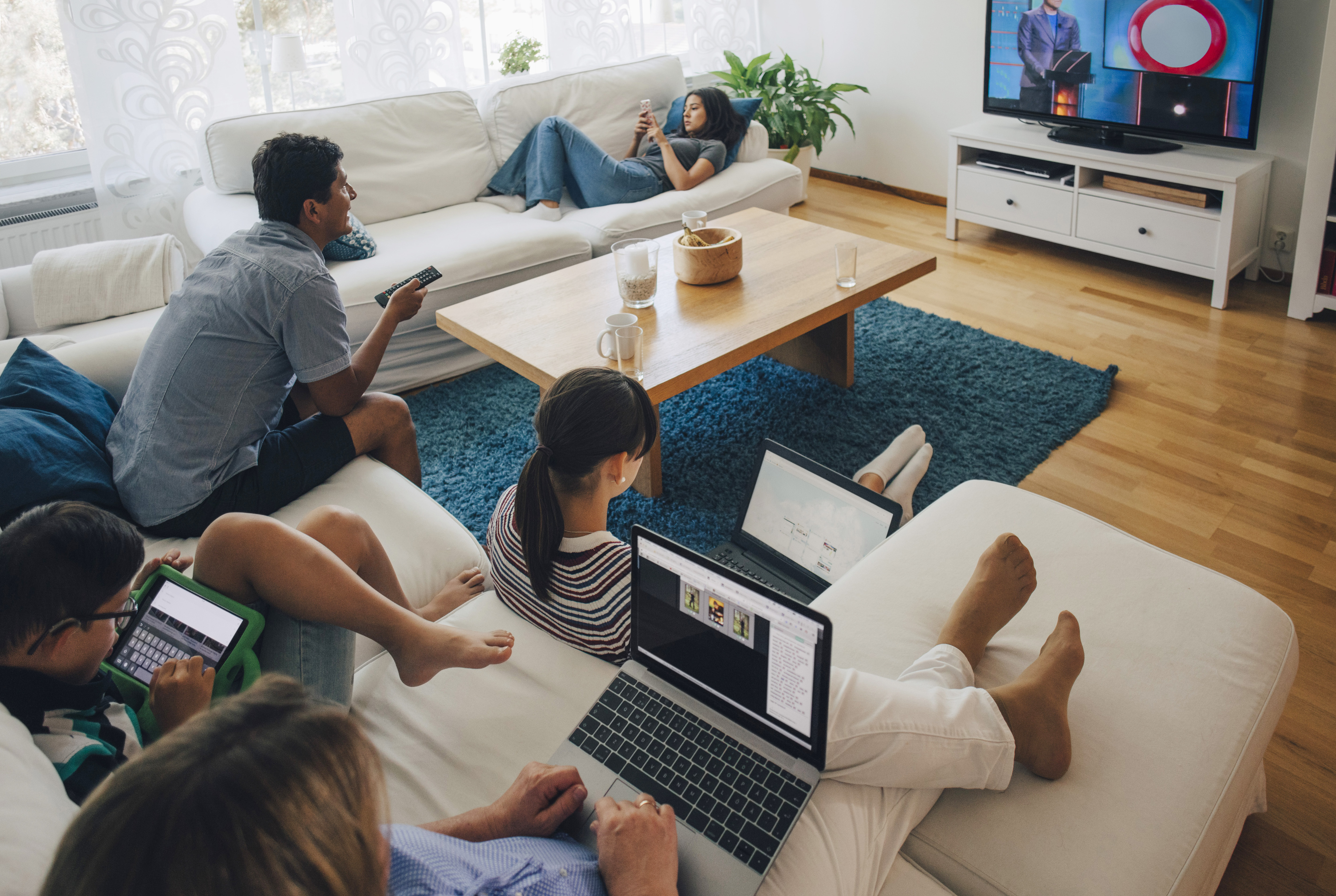 An overhead view of a family in a living room watching TV on multiple devices.