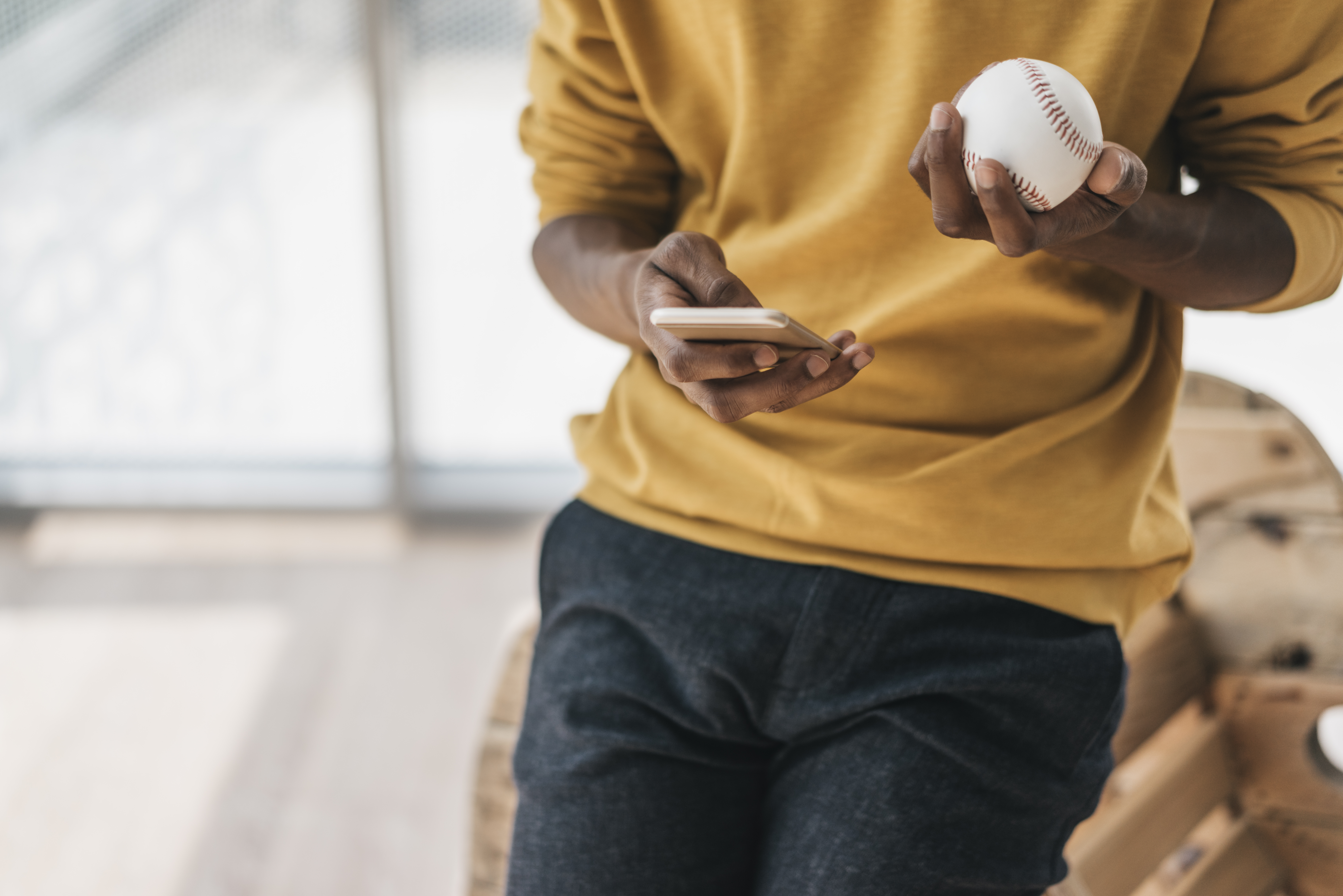 A closeup of a man holding a phone and a baseball.