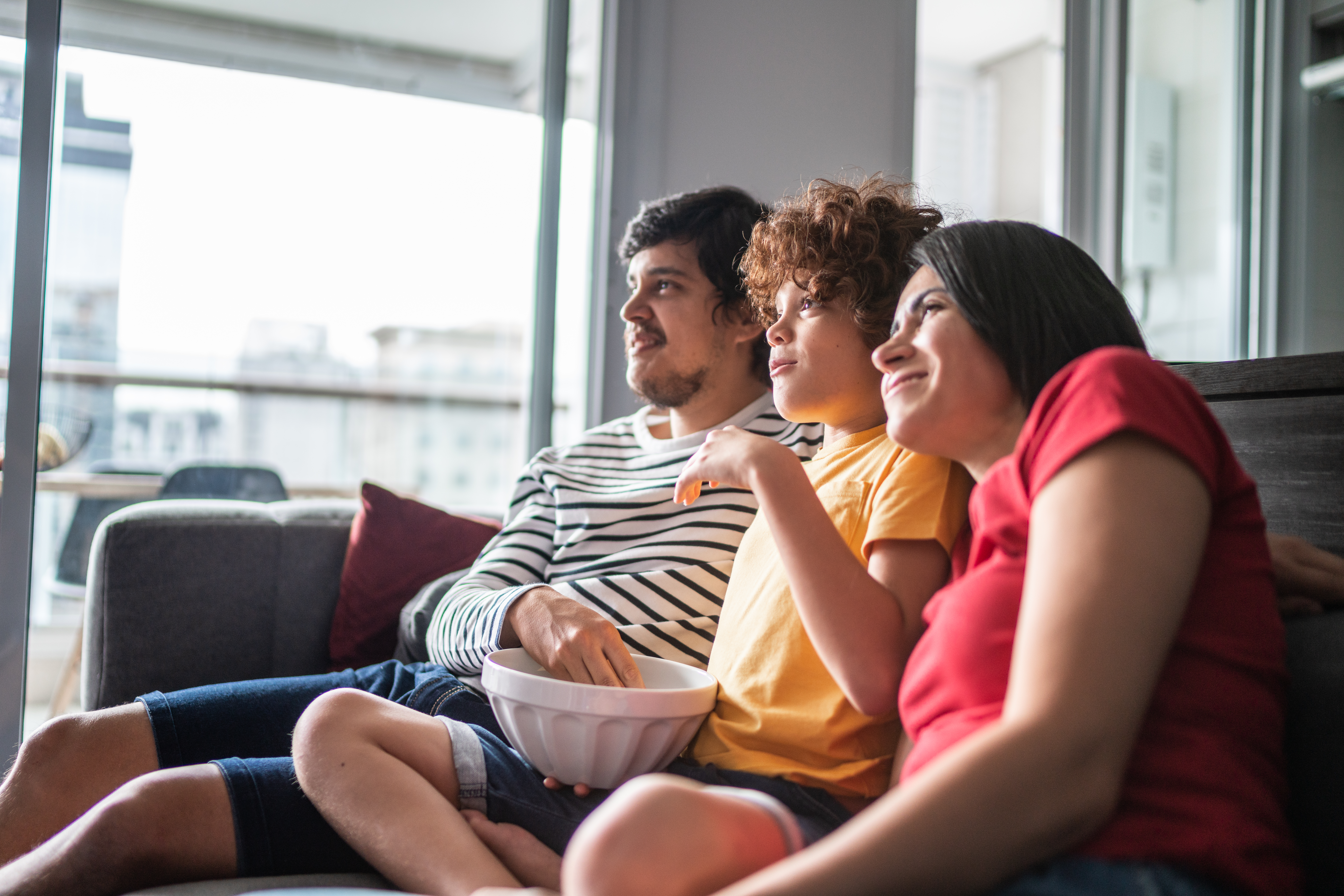 A closeup of a family sitting on a couch and eating popcorn