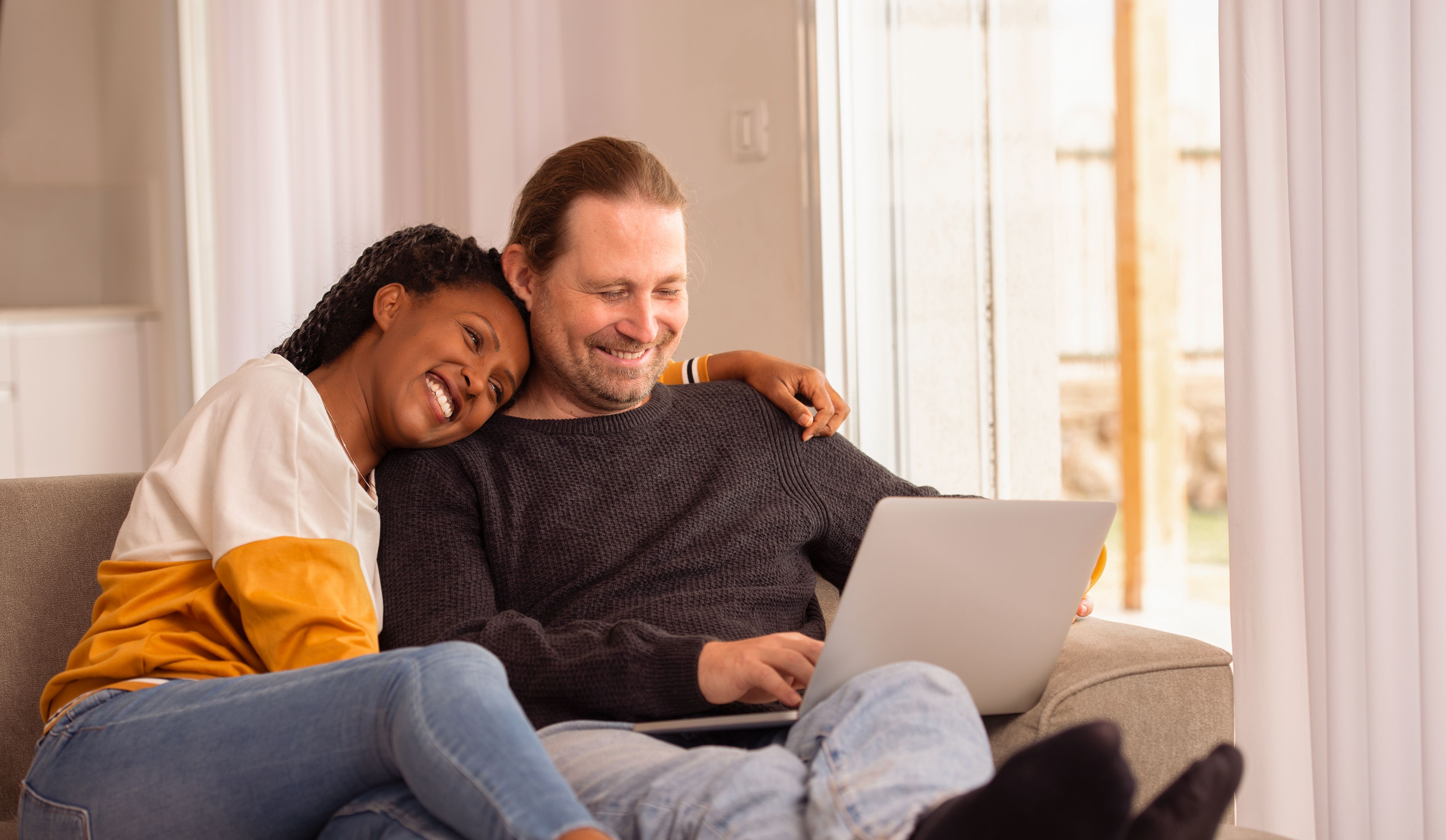 A young couple smiling and looking at a laptop together.