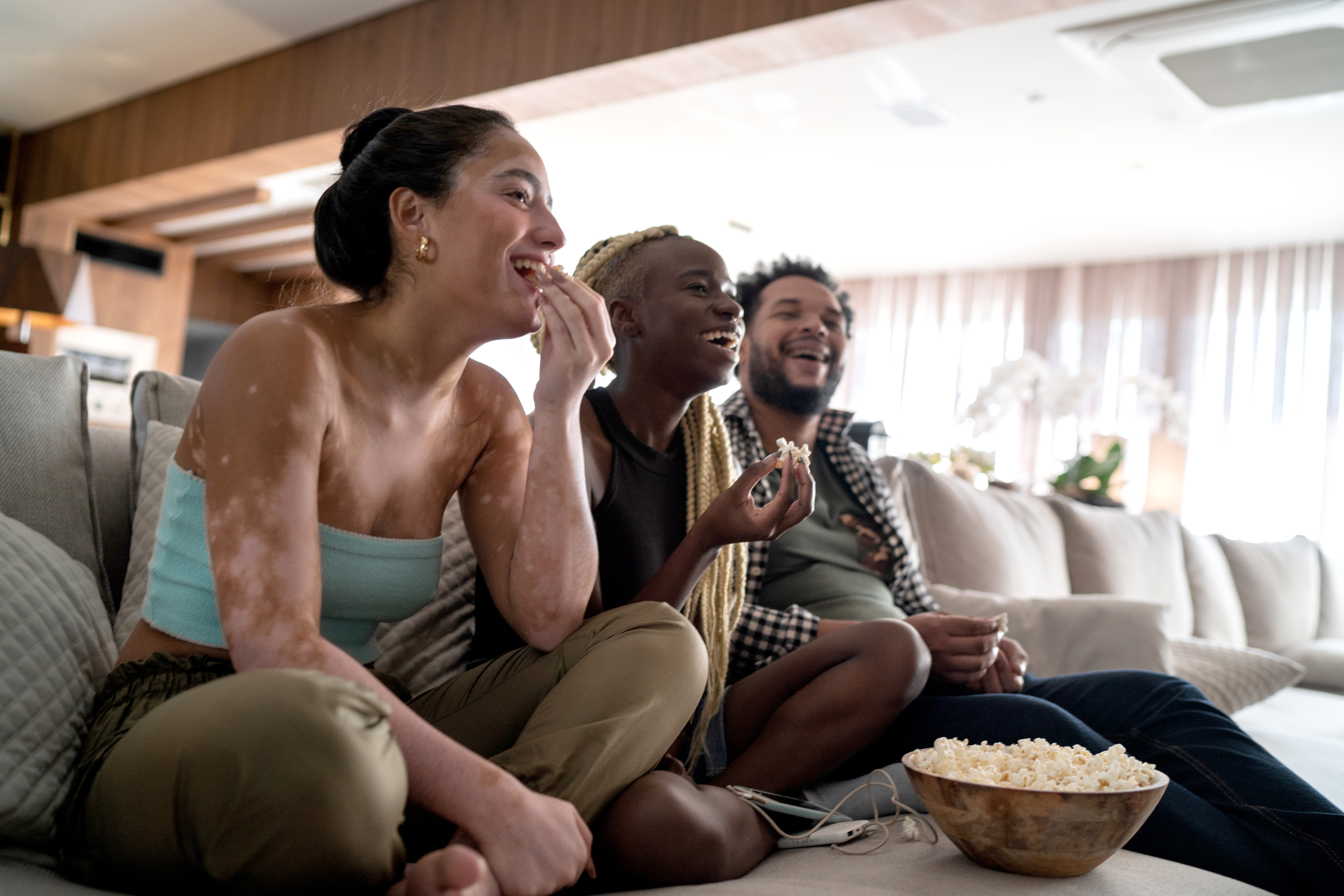 Three people sitting on a couch and snacking.