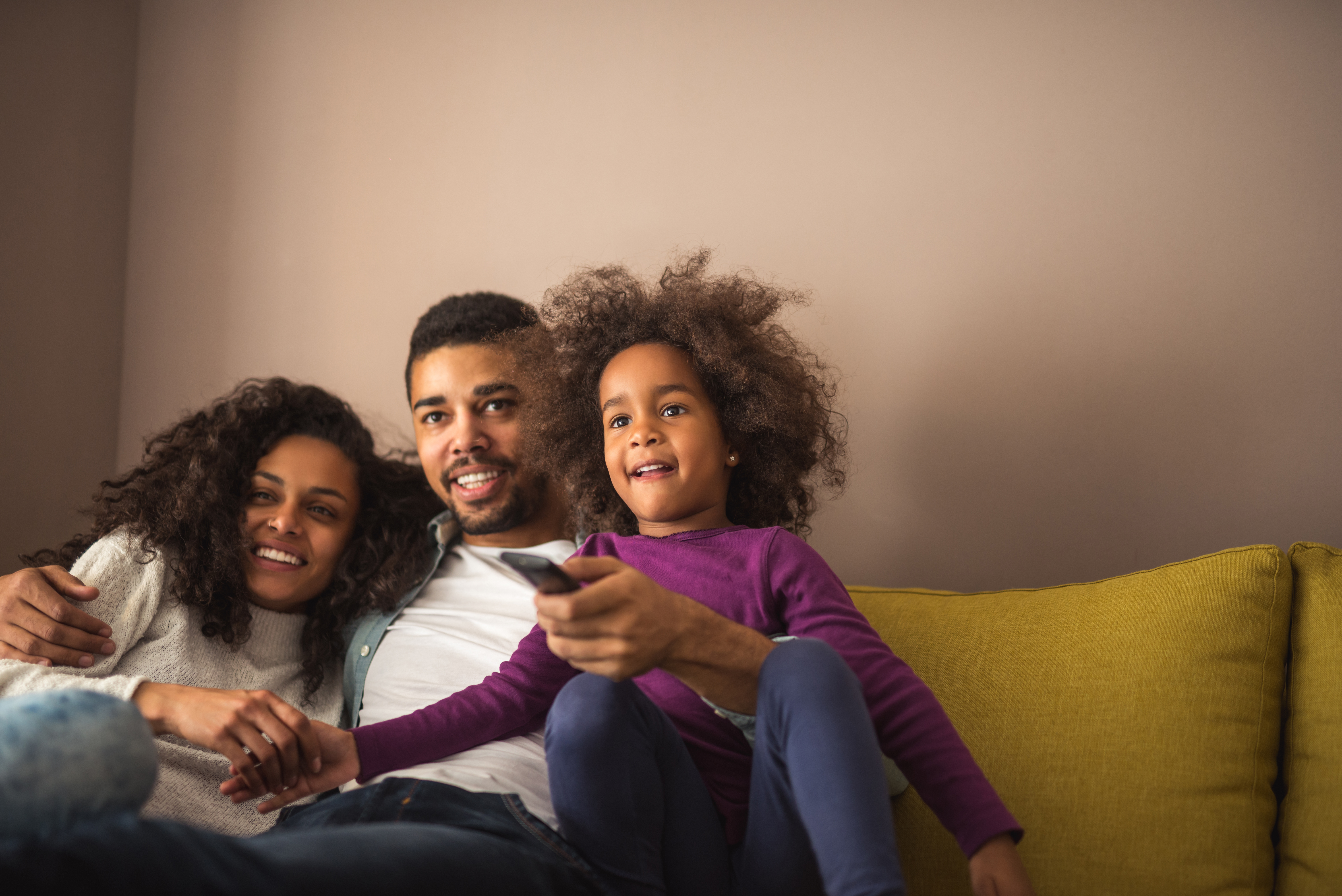 A family watching TV on a couch holding a remote.